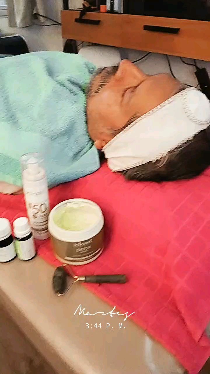 Una clienta con vincha blanca recostada en la camilla, con los productos del facial y un rodillo de jade delante